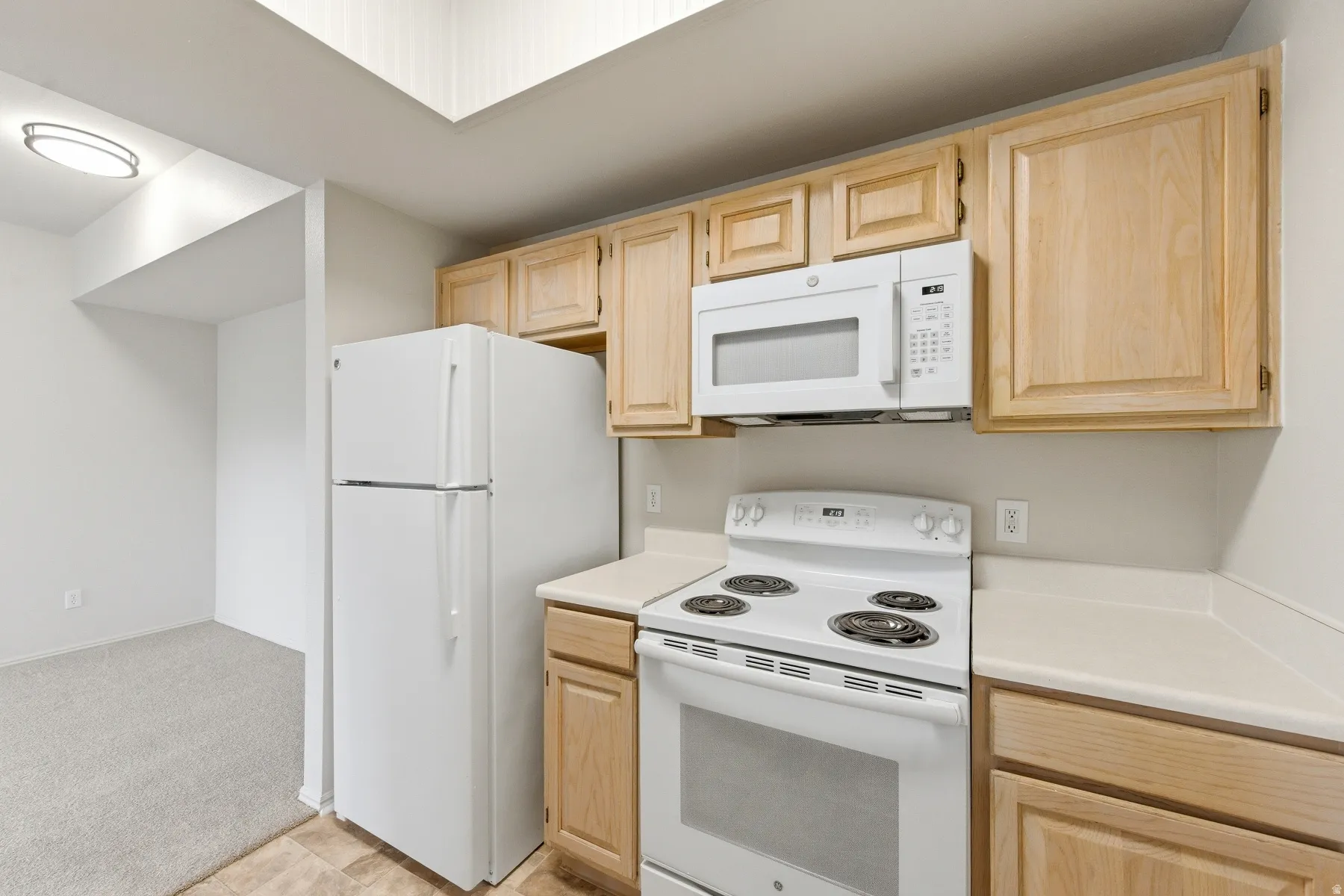 Kitchen featuring light wood cabinetry, white appliances, solid surface countertops, and tile flooring