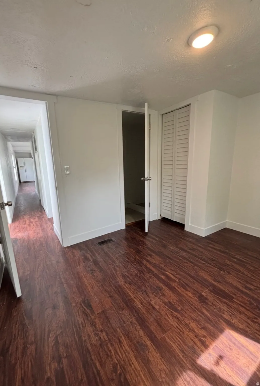 Interior room featuring wood-finish flooring, white walls, white trim, a flush-mount ceiling light, and a bi-fold closet door