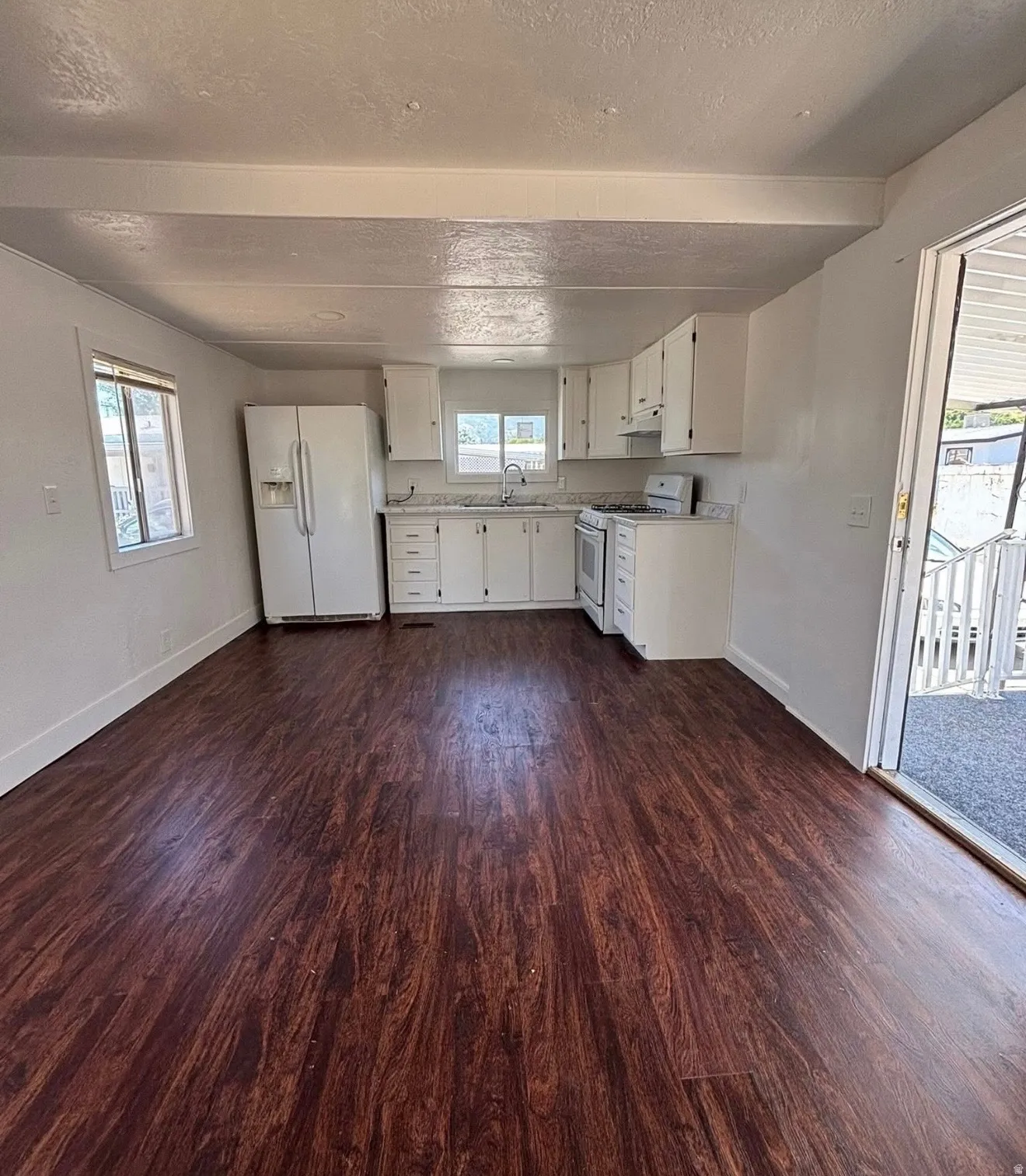 Open-concept living space featuring wood-finish flooring, white kitchen cabinetry, a built-in oven/range, and a side-by-side refrigerator