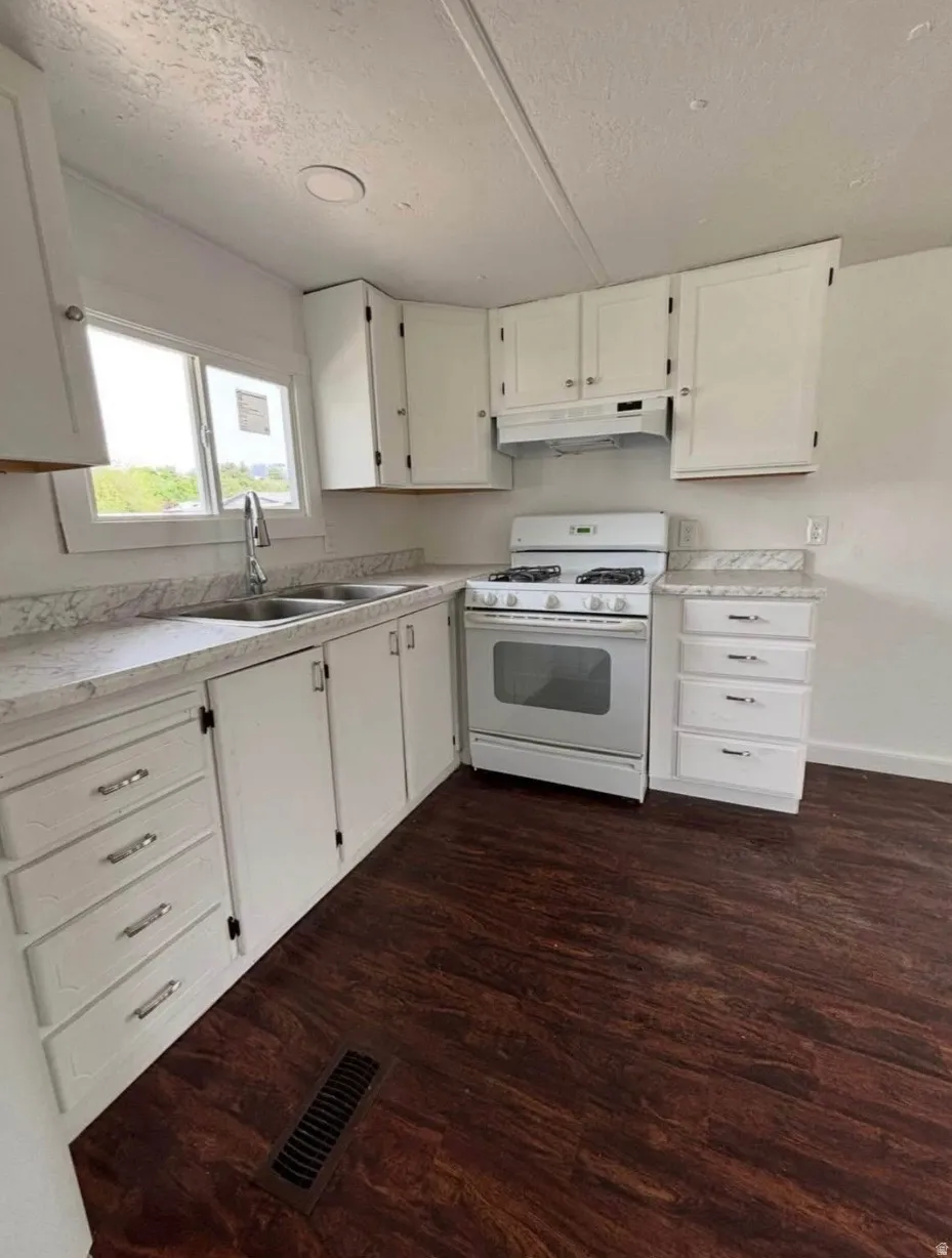 Kitchen featuring white cabinetry, white countertops, a double basin stainless steel sink, a white gas range, and dark wood-finish flooring