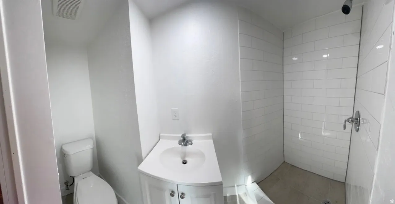 Modern bathroom featuring a white subway tile shower, a corner vanity with a round basin sink, and a white toilet