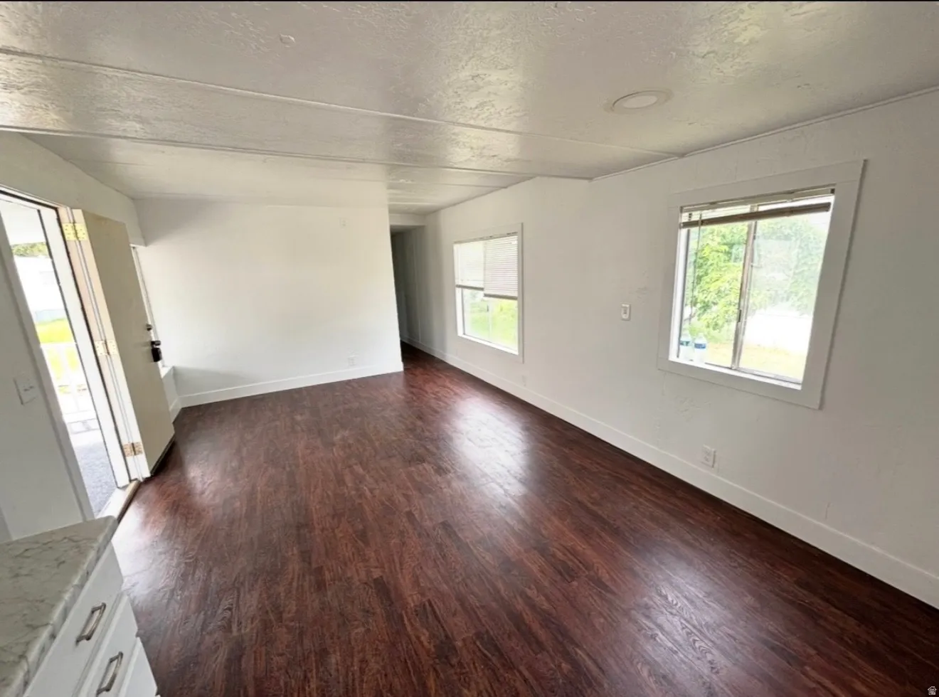 Spacious interior featuring rich wood-finish flooring, white walls, and multiple windows