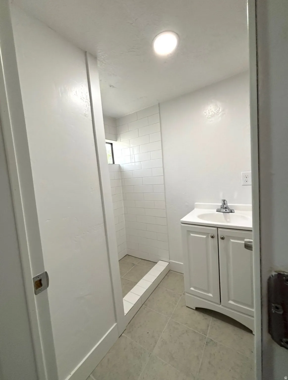 Contemporary bathroom featuring a subway-tiled shower, white vanity with integrated sink, chrome faucet, and recessed ceiling lighting