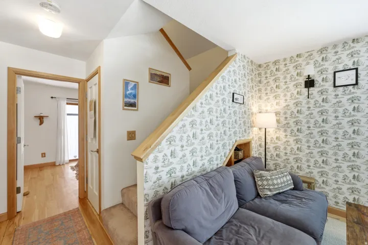 Carpeted staircase with light wood handrail, built-in shelving, and patterned wallpaper