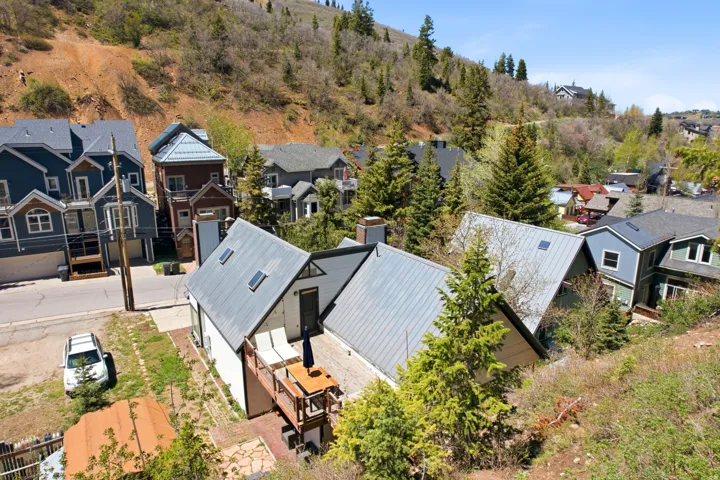 Property featuring a metal roof, an exterior deck, and skylights, set against a backdrop of natural hillside landscaping and mature evergreen trees