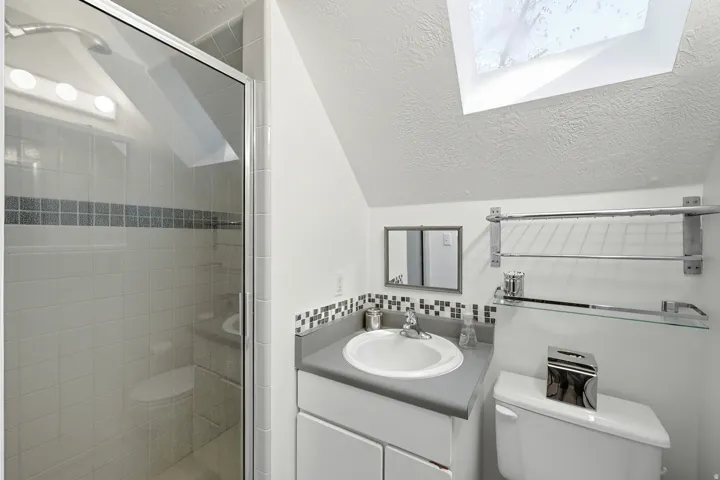 Bathroom featuring a glass-enclosed shower, white tile surround with decorative accent band, and a vanity with an integrated sink