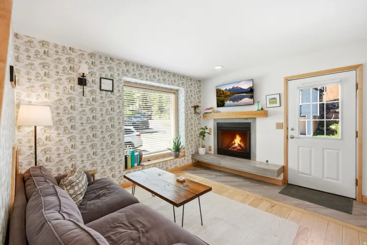 Living area featuring a built-in fireplace with a light wood mantle, a wide window with horizontal blinds, and a white entry door with a multi-pane window insert