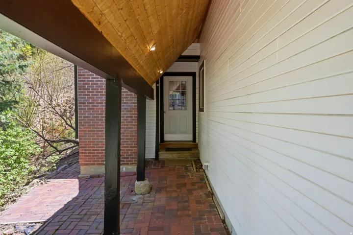 Covered entry with exposed wood ceiling, recessed lighting, and brick paver flooring
