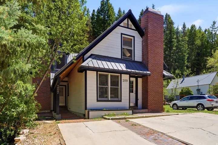 Gabled facade featuring white siding, a metal roof, and a prominent brick chimney
