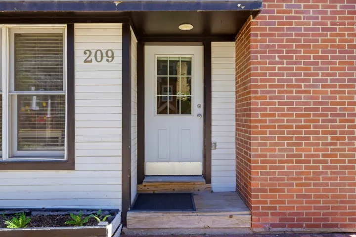 Entryway featuring a white door with window panes, wood siding, brick exterior, and a built-in planter box