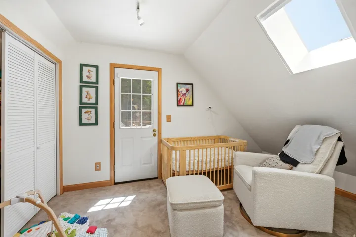 Angled ceiling room with a skylight, white louvered bifold closet doors, a paneled door with window inserts, track lighting, and wood-finish trim