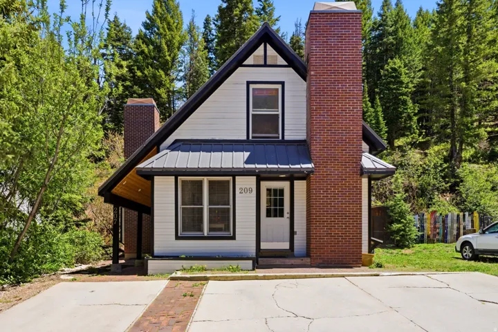 Gabled home featuring white siding with black trim, a standing seam metal roof, and two brick chimneys