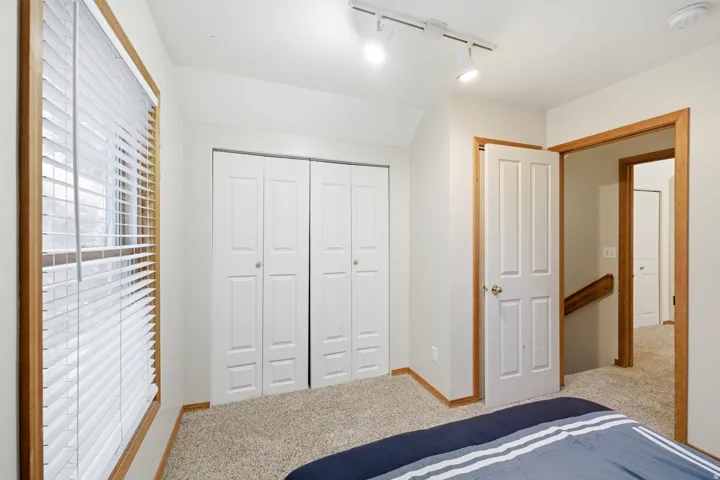 Carpeted room featuring a window with wood trim, white blinds, and white bi-fold closet doors