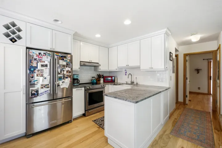 Kitchen featuring white cabinetry, stainless steel appliances, granite countertops, a white subway tile backsplash, and wood-finish flooring