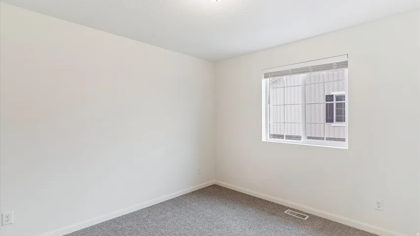 Interior room featuring neutral wall paint, gray carpet, a single window with horizontal blinds, and a ceiling-mounted light fixture