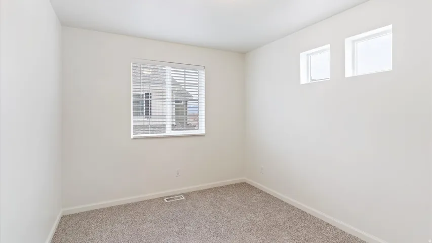 Neutral-toned room featuring a large window with blinds, two high-set windows, white baseboards, and neutral carpet flooring