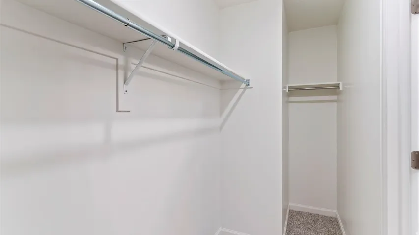 Walk-in closet featuring white walls, shelving, and metal hanging rods