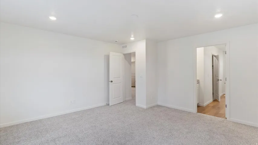Spacious interior room featuring light gray carpeting, white walls, recessed ceiling lighting, and two panel doors