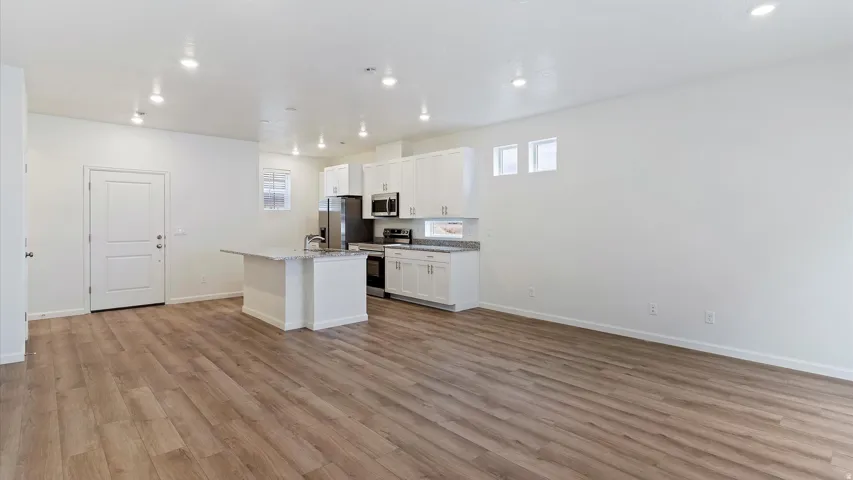 Open-concept living area with wood-finish flooring, recessed lighting, and a kitchen featuring white cabinetry, a central island with a breakfast bar, and stainless steel appliances