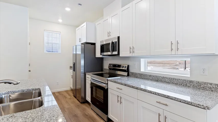 Modern kitchen featuring white cabinetry, stainless steel appliances, granite countertops, wood-finish flooring, and a double basin sink