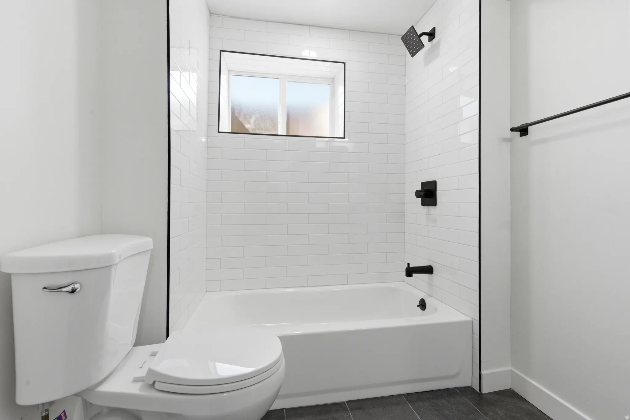 White subway tile bath surround featuring a black framed window and matte black fixtures