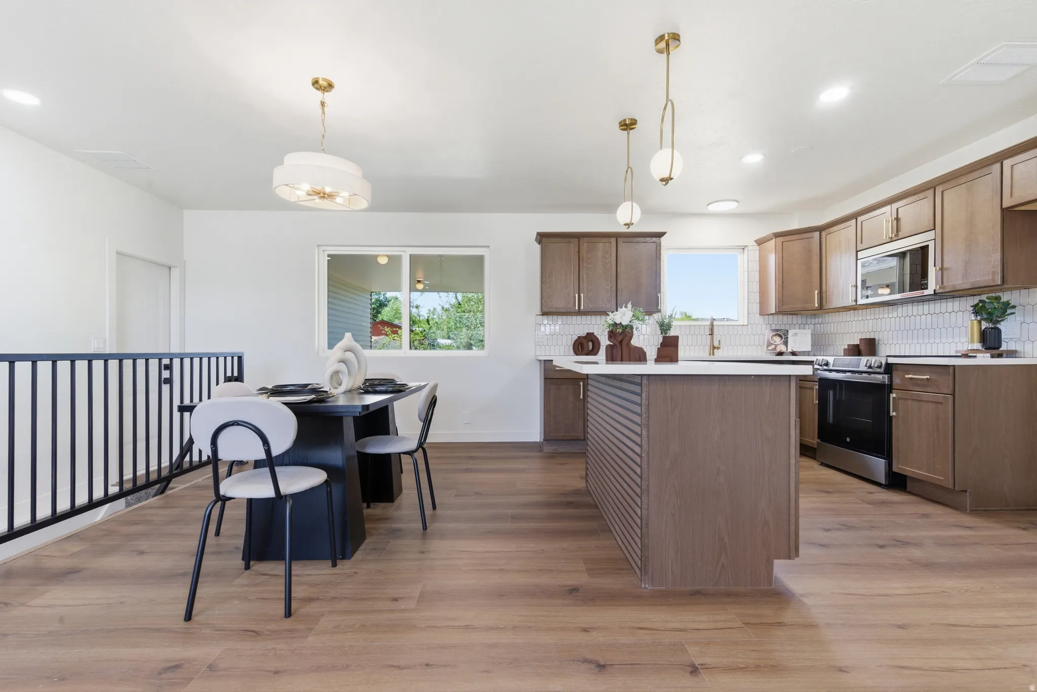Open-concept kitchen and dining area featuring wood-finish flooring, recessed lighting, and a black metal railing