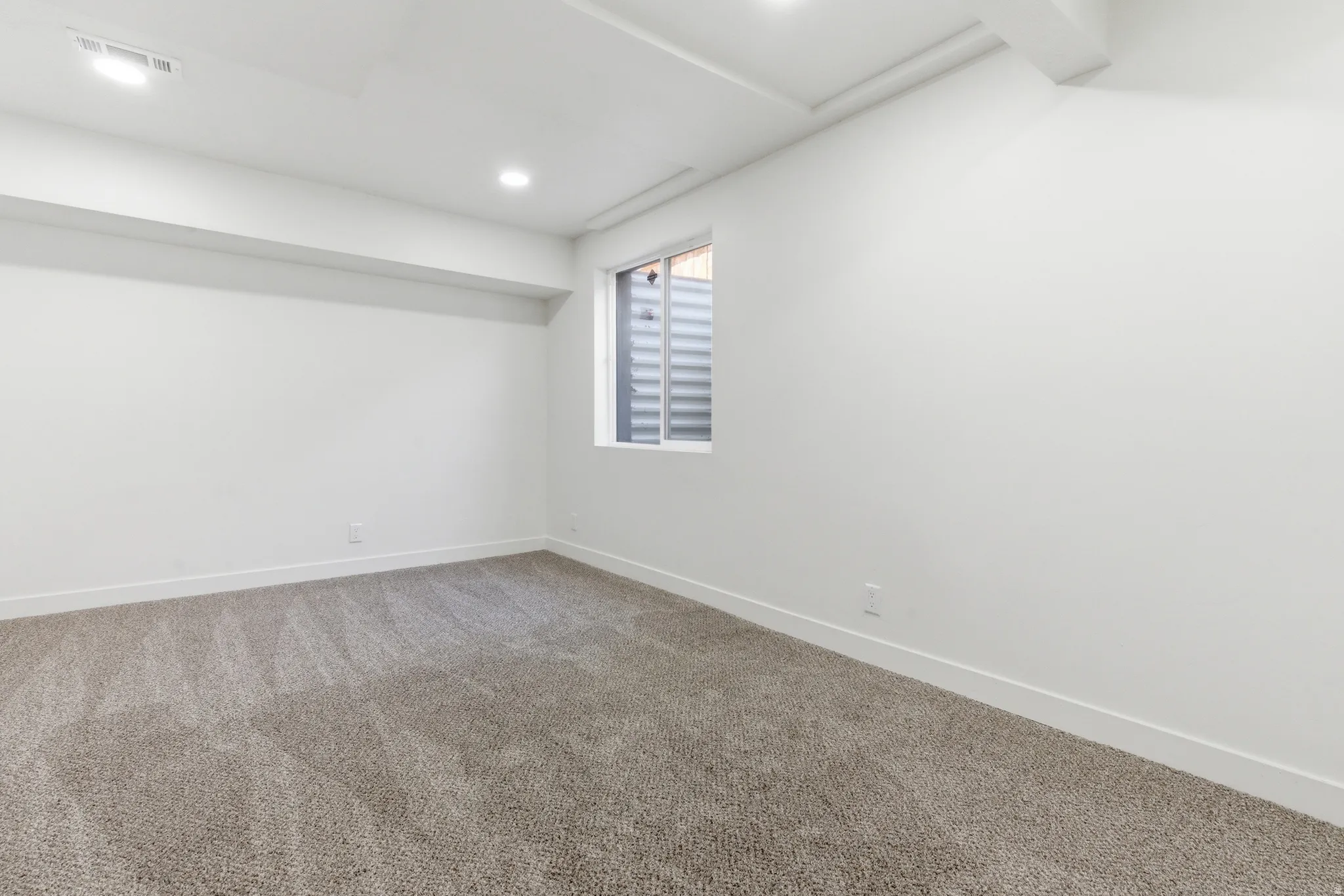 Spacious room featuring neutral carpeting, white walls, recessed lighting, and a window with a window well