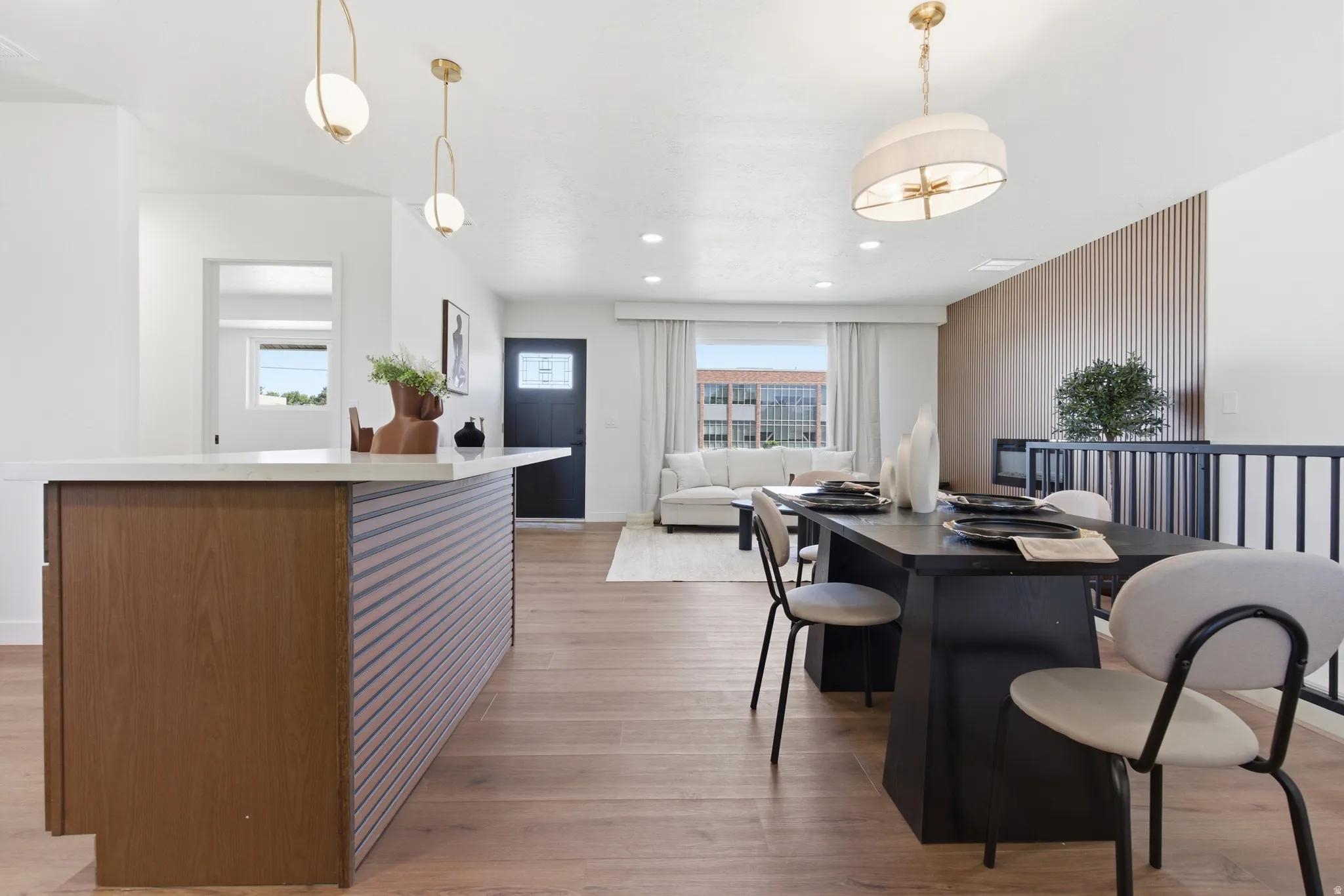 Open-concept living area with wood-finish flooring, a kitchen island featuring a light-toned countertop, and a dining area illuminated by a drum pendant light