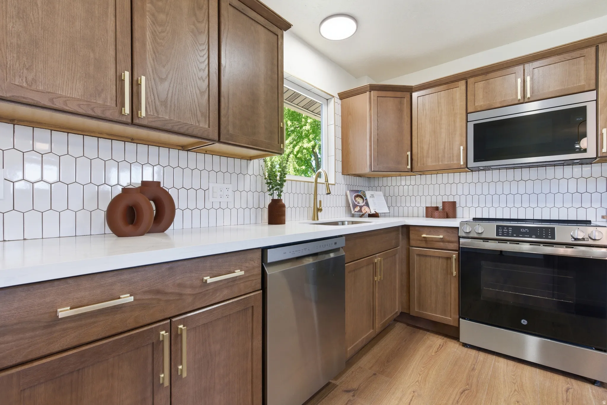 Kitchen featuring wood-finish cabinetry, white solid surface countertops, and an elongated hexagon tile backsplash