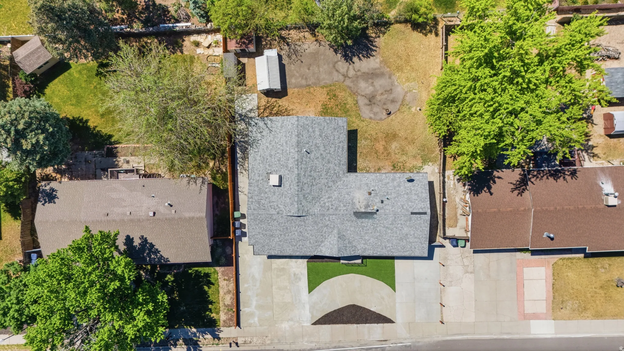 Shingle roof residence featuring a concrete driveway, partial artificial turf landscaping, and mature trees