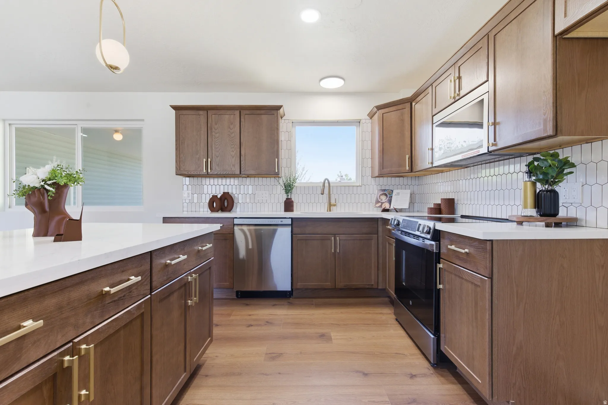 Modern kitchen featuring wood-finish cabinetry with brass hardware, white countertops, and a white picket tile backsplash