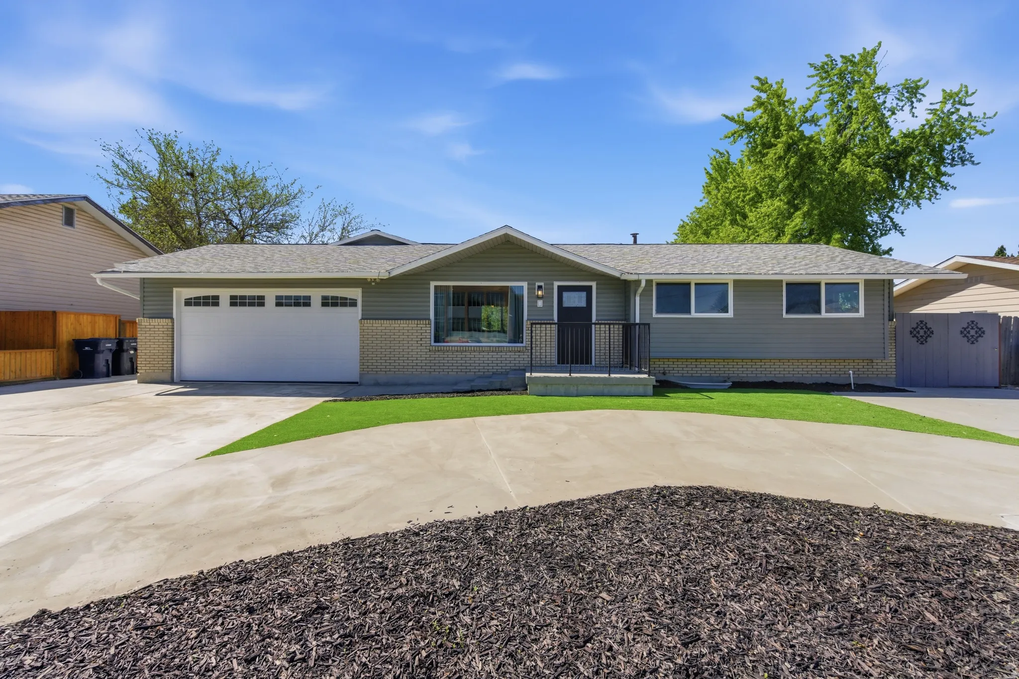 Ranch-style exterior featuring gray siding, light brick detailing, and a white garage door with upper window inserts