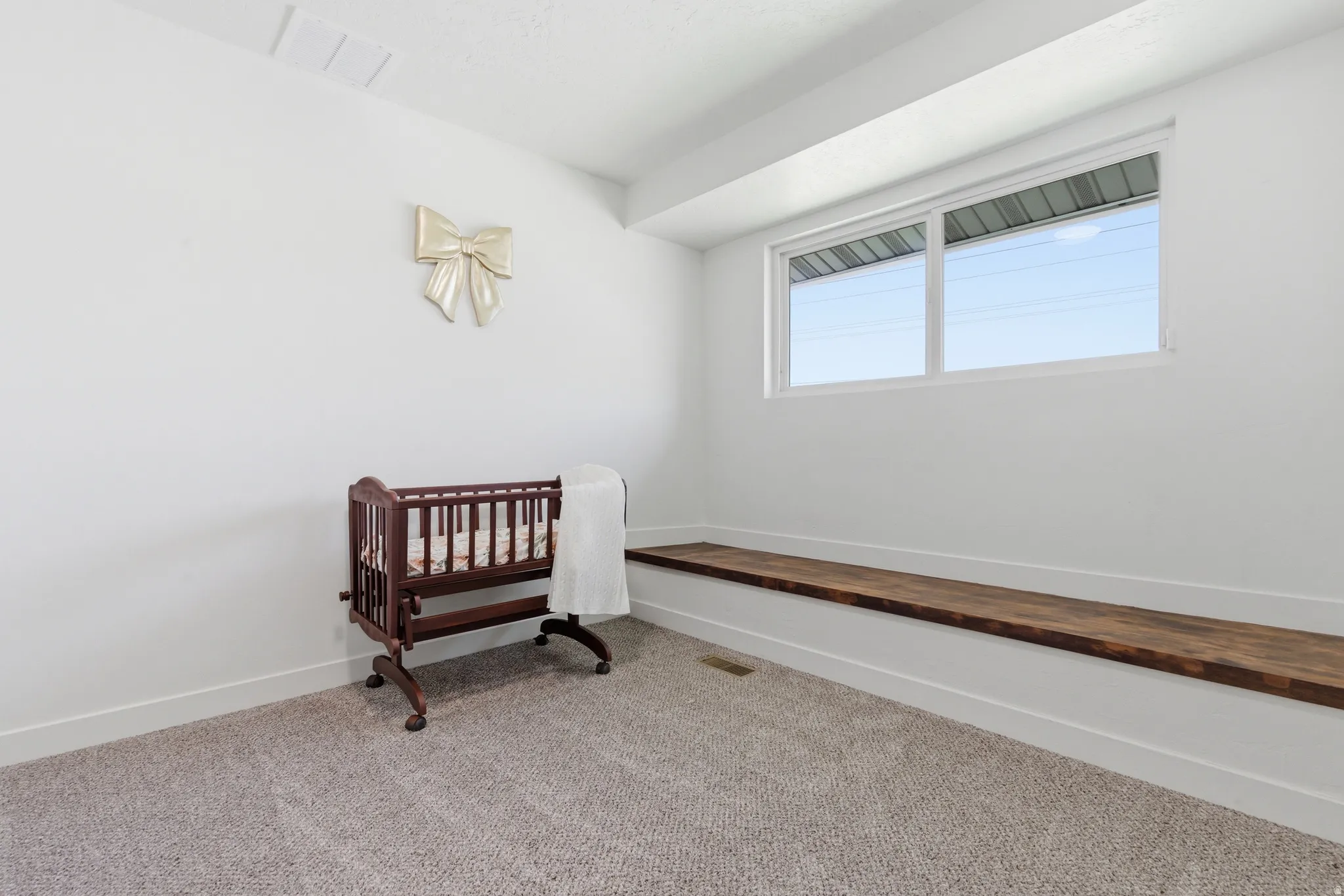 Carpeted room featuring a window with a wood-finish bench below, white walls, and white trim