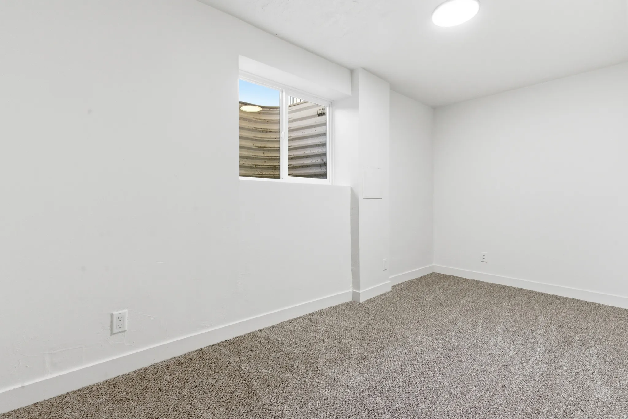 Spacious room featuring neutral carpeting, white walls, a single window, and a flush-mount ceiling light fixture