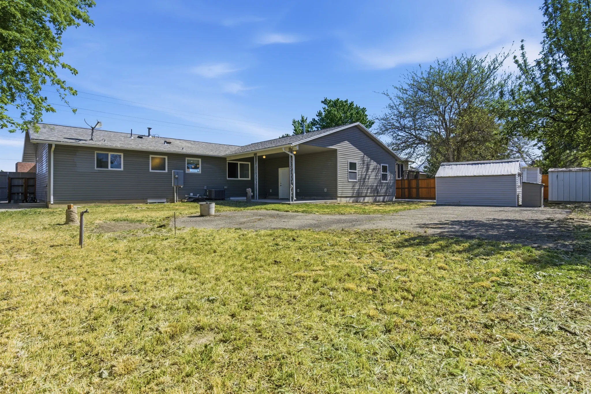 Expansive property featuring a single-story residence with gray siding, multiple windows, and a covered patio area