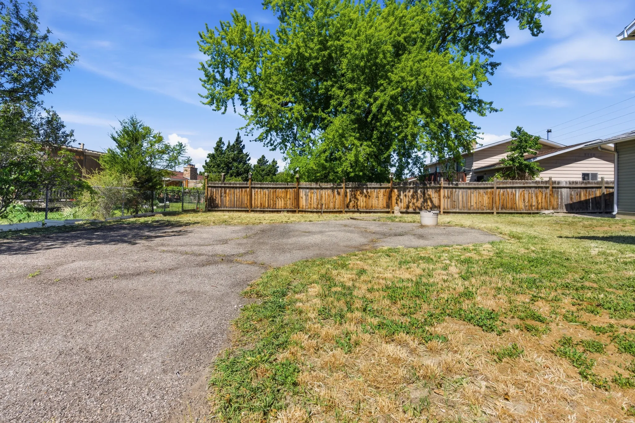 Expansive backyard with a large concrete patio, surrounded by a wood privacy fence and mature trees