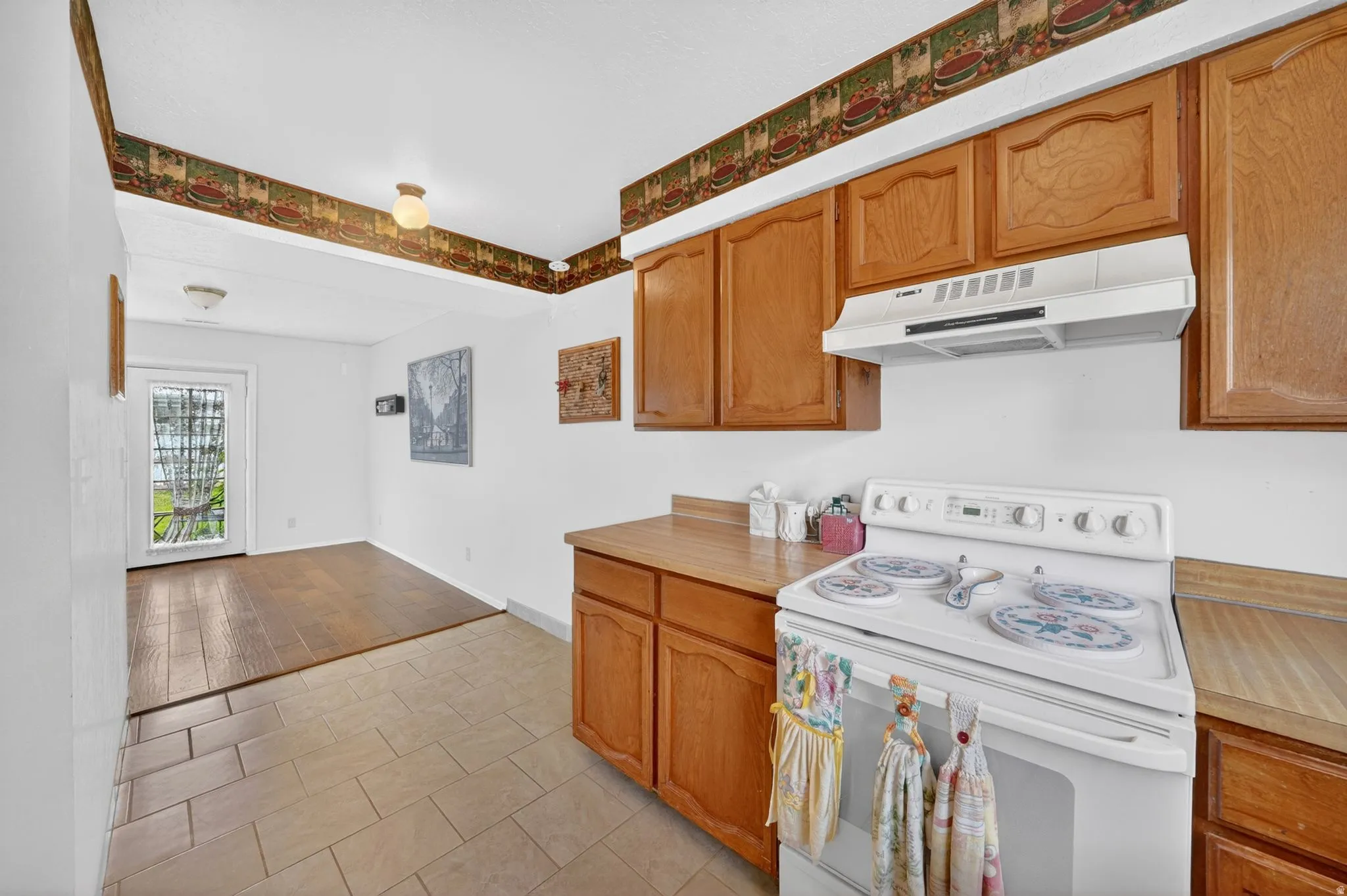Kitchen featuring wood-finish cabinetry, laminate countertops, and a white electric range with an overhead vent