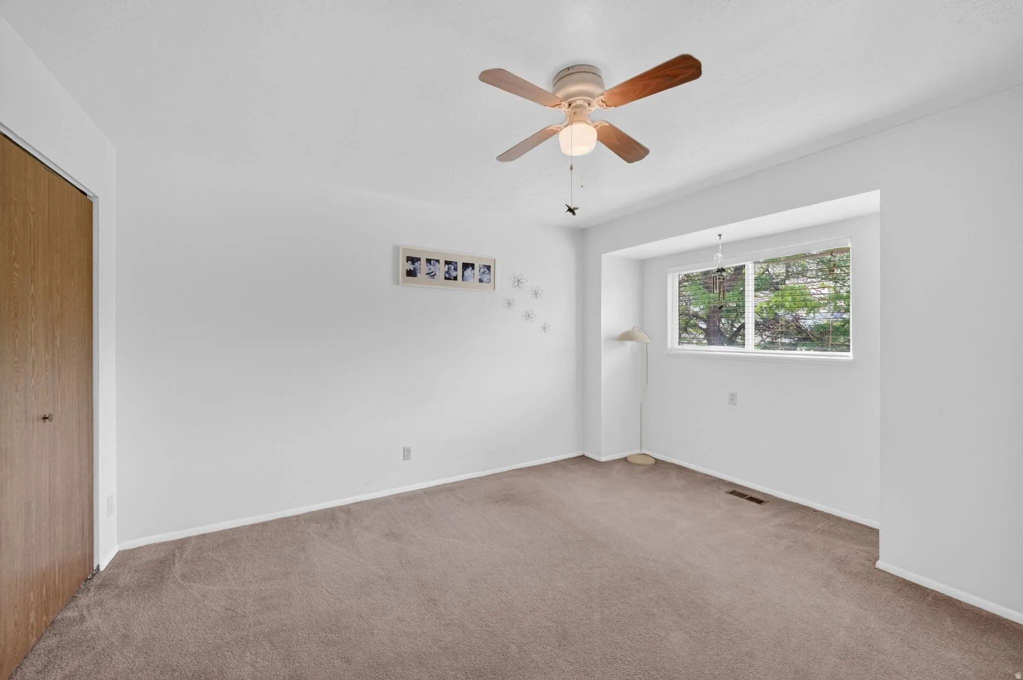 Carpeted room featuring a ceiling fan with light fixture, a window alcove, and a wood-finish bi-fold closet door