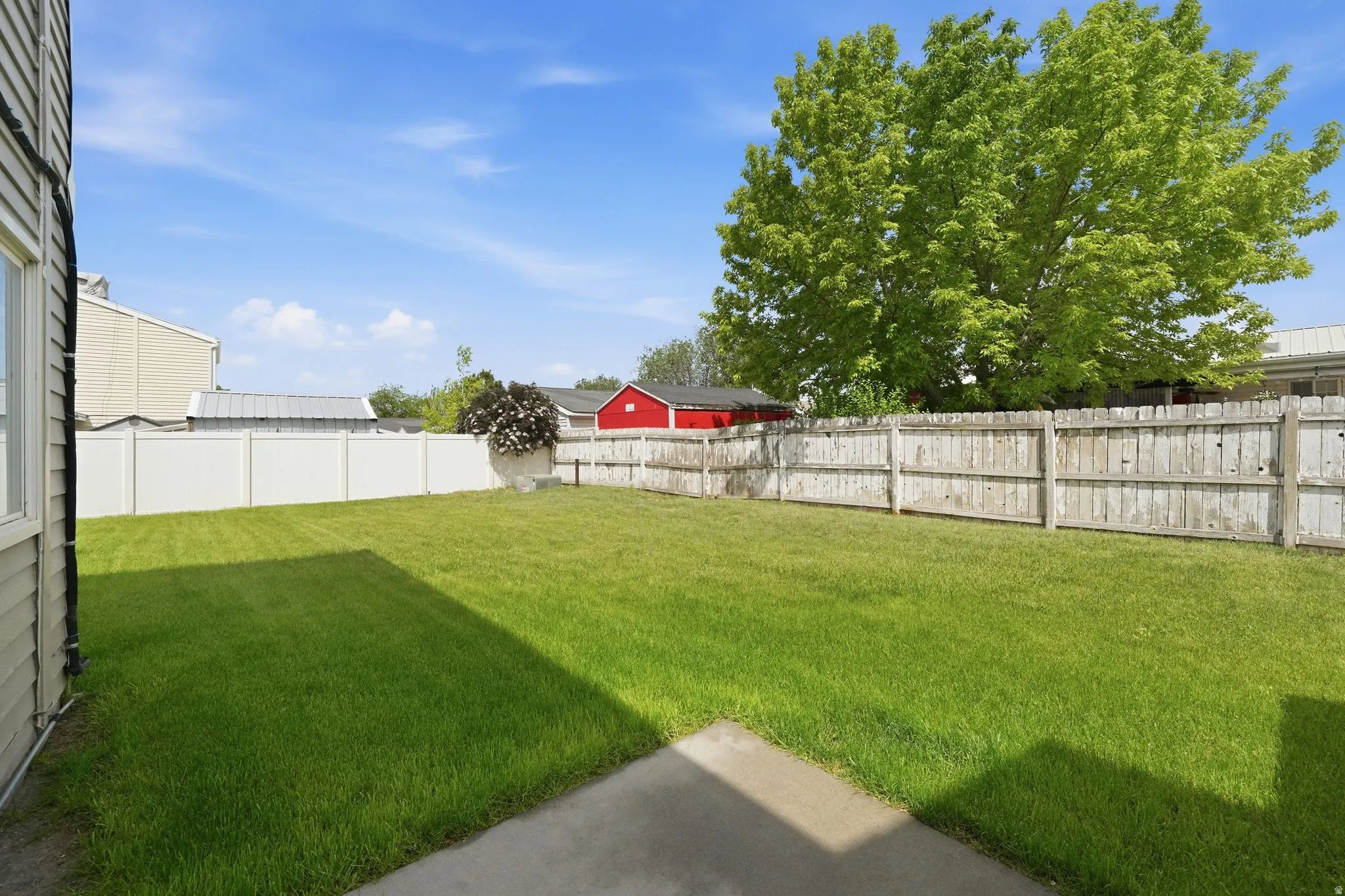 Expansive green lawn featuring a concrete patio, a combination of vinyl and wood fencing, and mature trees providing natural shade