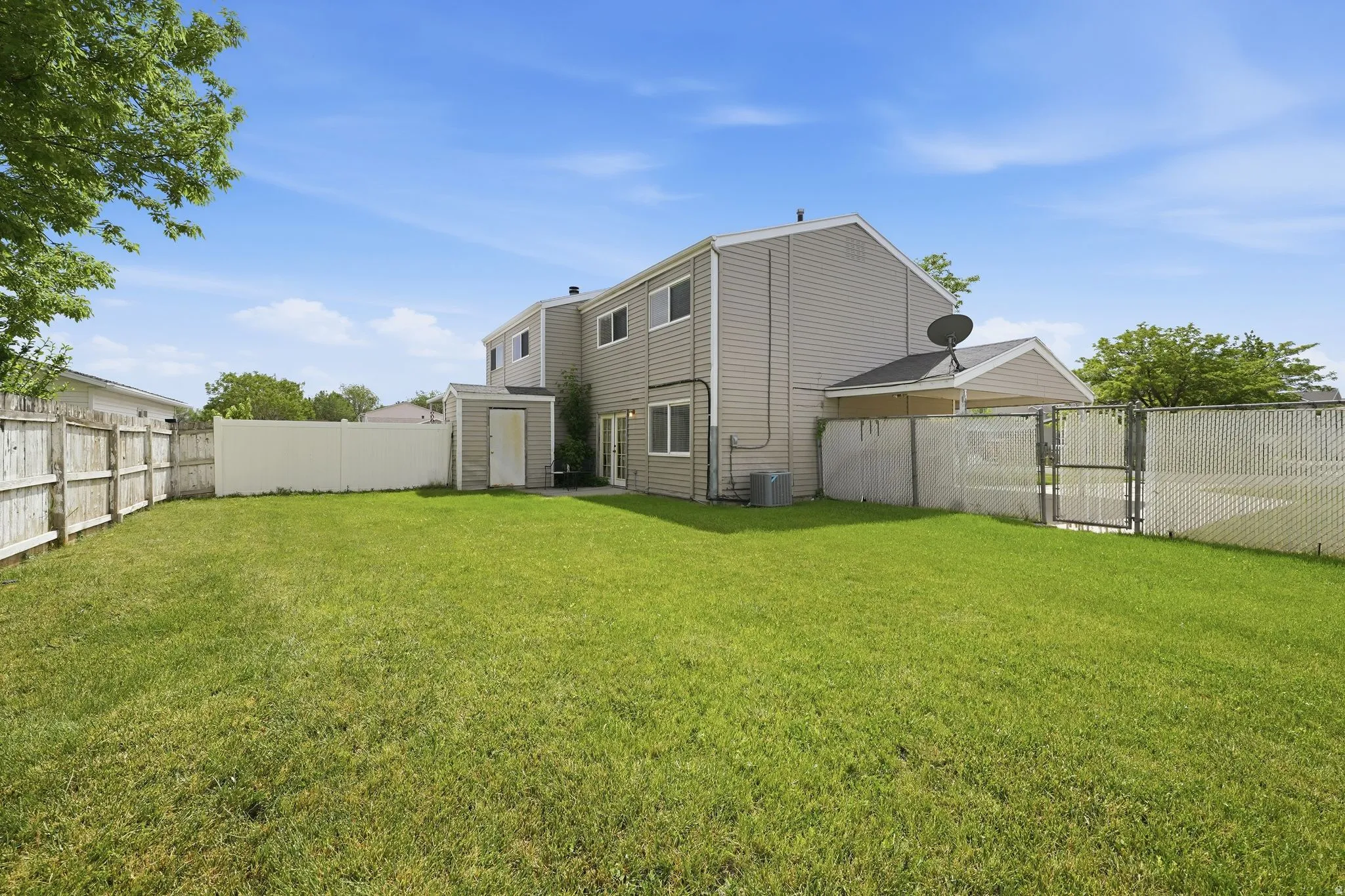 Expansive grassy backyard featuring a storage shed, white vinyl privacy fencing, and a partial chain-link fence with a gate