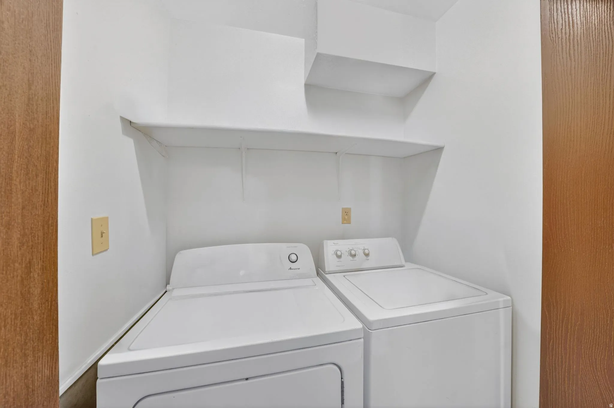 Dedicated laundry area featuring a white top-load washer and dryer set, built-in shelving, and a wood-finish door frame