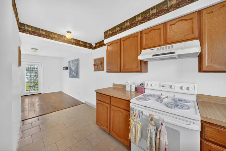 Kitchen featuring wood-finish cabinetry, laminate countertops, and a white electric range with an overhead vent