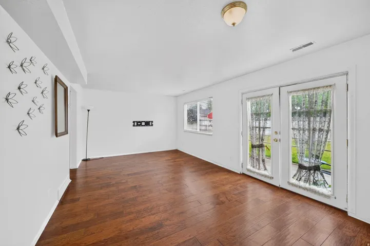 Spacious room featuring wood-finish flooring, white walls, and bright overhead lighting
