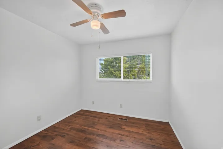 Bright room featuring wood-finish flooring, a white ceiling fan with light fixture, and a large window with blinds