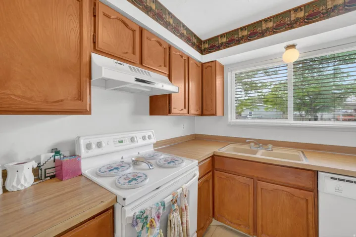 Kitchen featuring wood cabinetry, wood-finish countertops, white electric range with range hood, and a dual basin sink with window