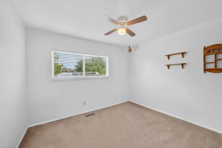 Spacious room with plush carpeting, a large window, and a ceiling fan with light fixture