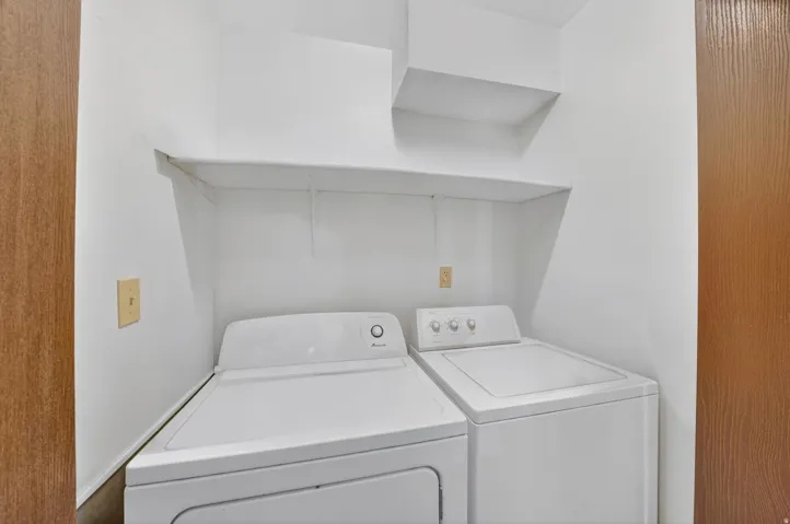 Dedicated laundry area featuring a white top-load washer and dryer set, built-in shelving, and a wood-finish door frame