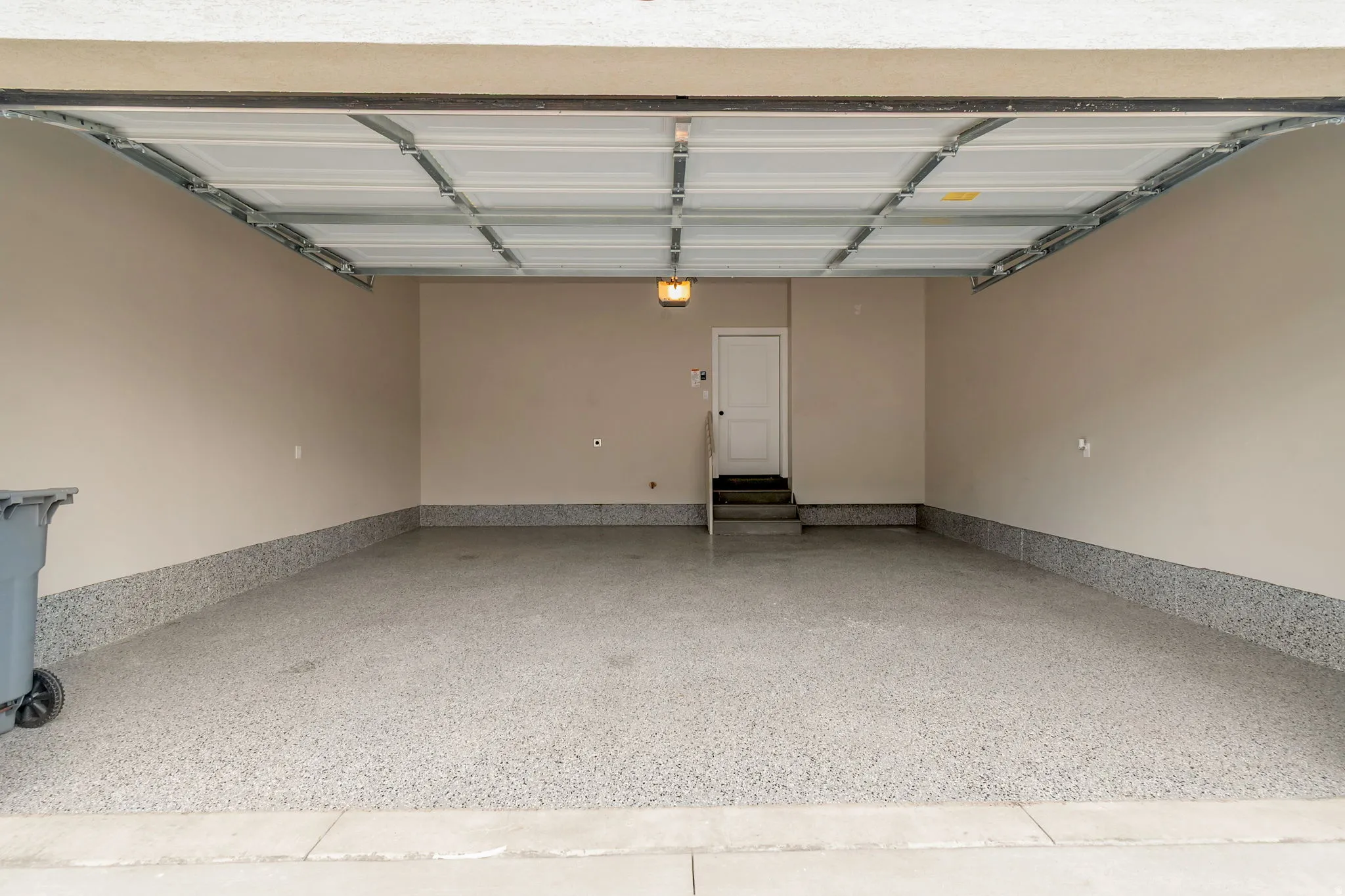 Spacious garage featuring a finished epoxy floor, neutral painted walls, overhead lighting, and a white interior door with steps