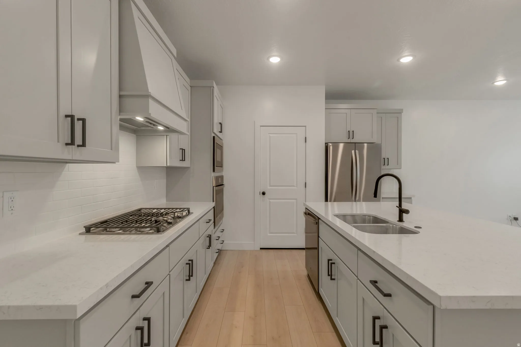 Modern kitchen featuring light-toned cabinetry with dark hardware, a center island with an undermount sink and matte black faucet, and light wood-finish flooring