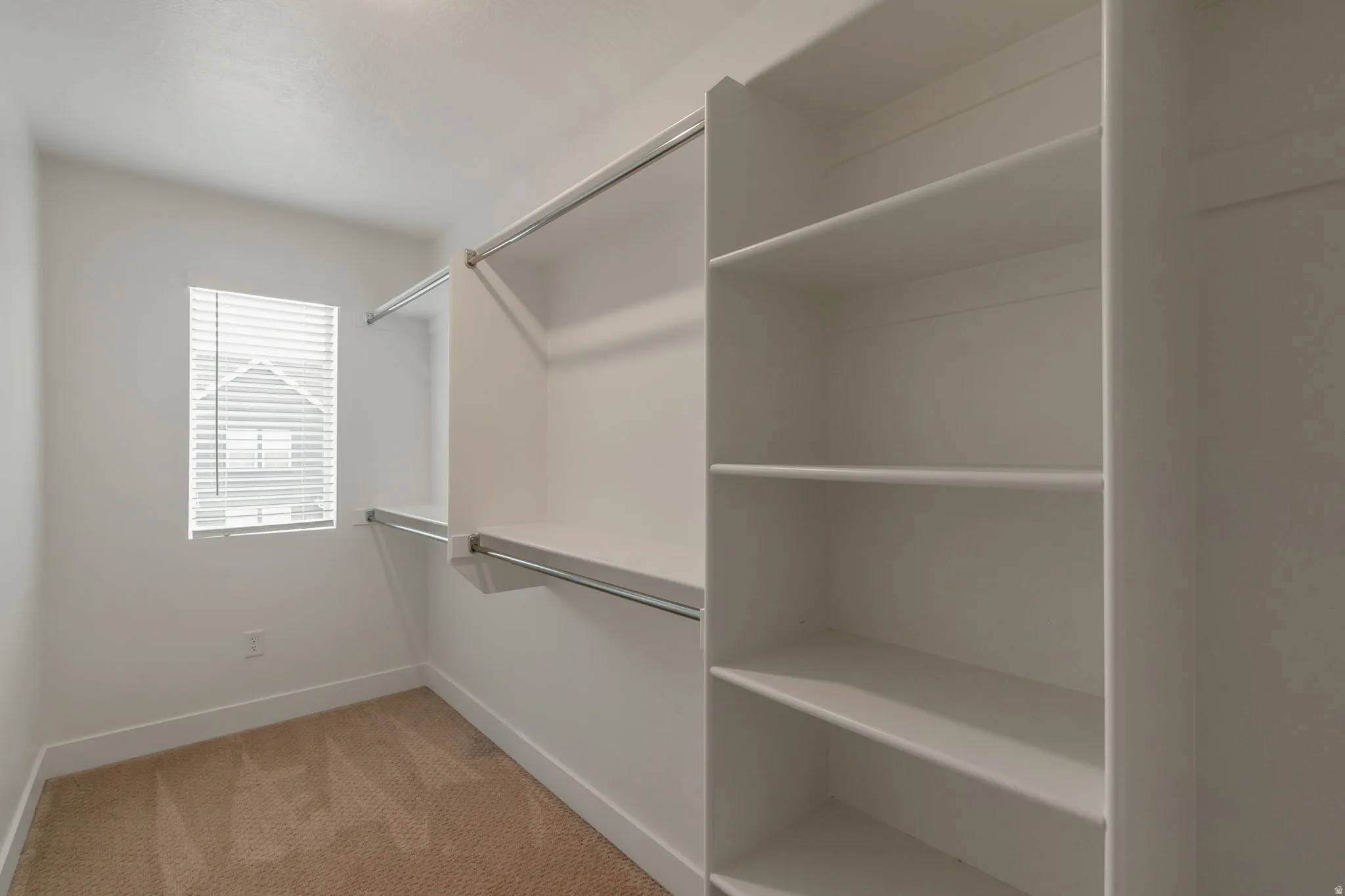 Walk-in closet featuring built-in shelving, dual hanging rods, and a window with blinds